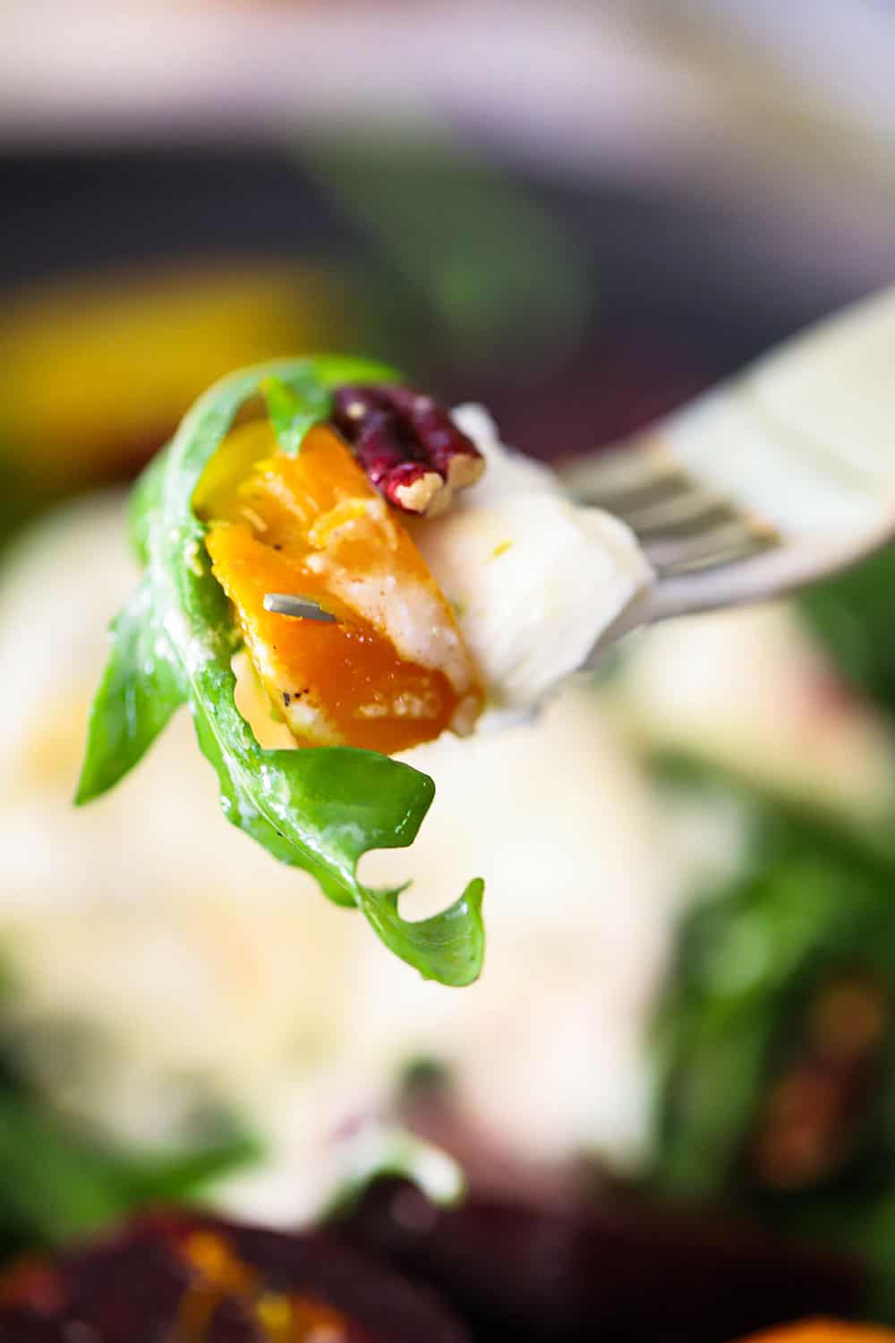 A fork holding up a piece of burrata cheese, roasted golden beet, and arugula salad. 