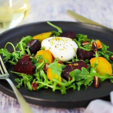 A dark circular plate filled with roasted beet and burrata salad.