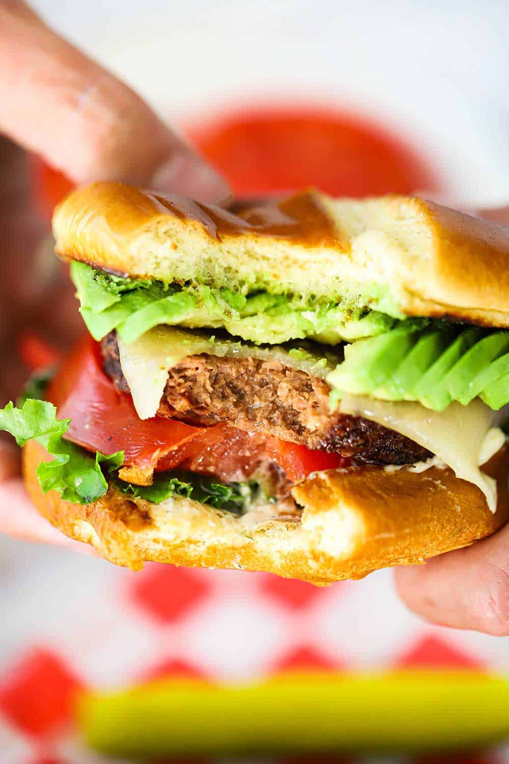 Two hands holding a plant-based California burger with a bite taken out of it. 