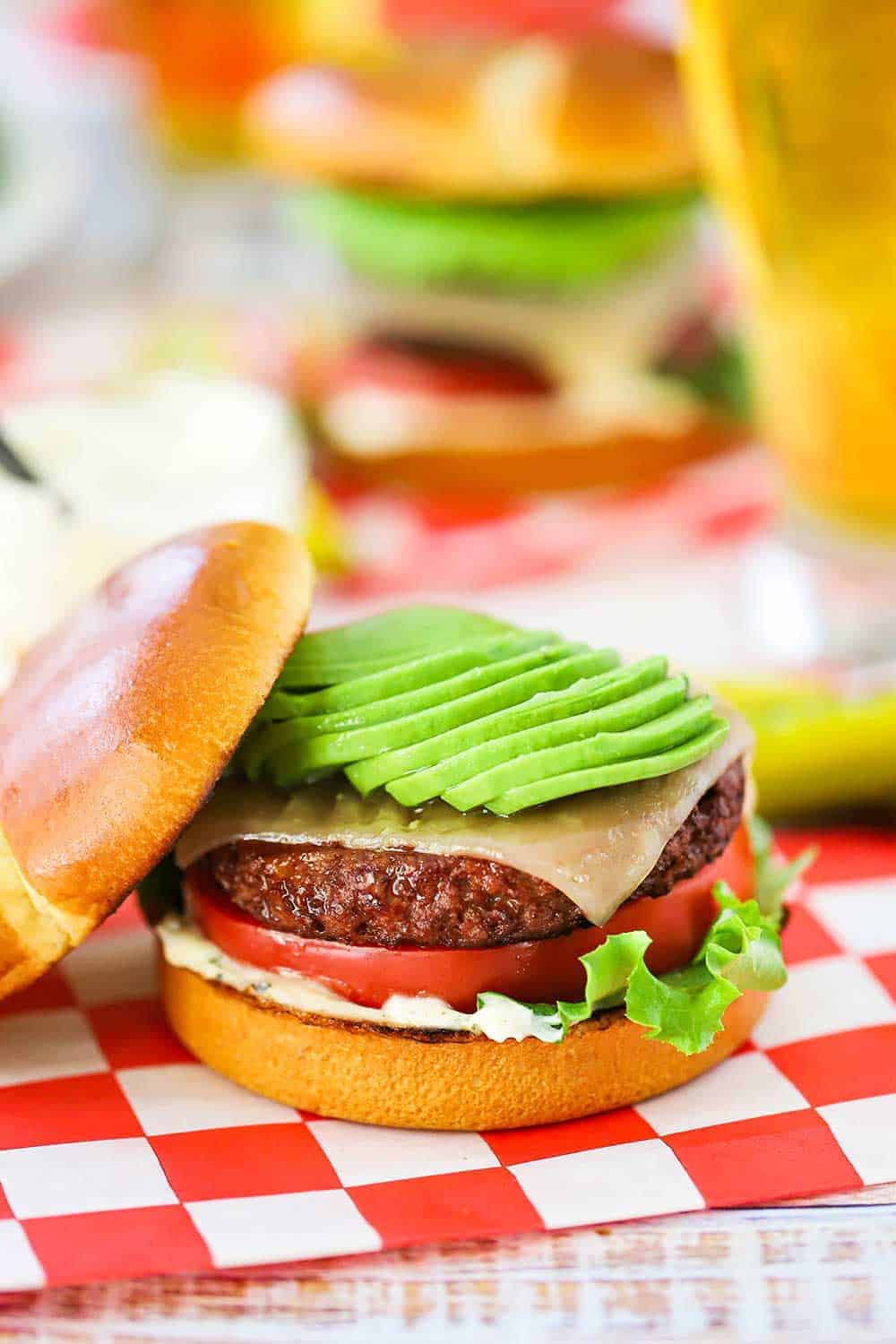 A plant-based California burger topped with sliced avocado sitting on a red-checkered napkin. 