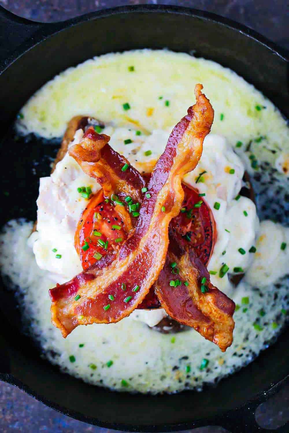 A Kentucky hot brown topped with two strips of bacon all in a cast iron skillet. 