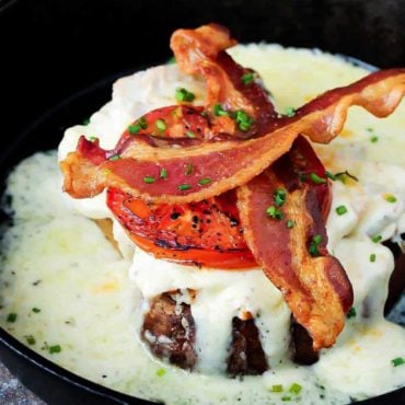 A Kentucky hot brown topped with two strips of bacon all in a cast iron skillet.