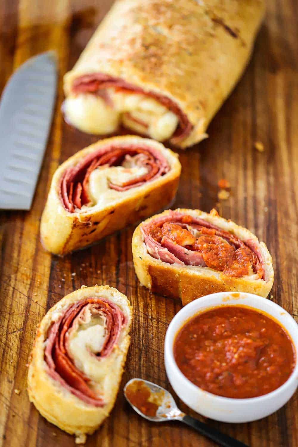 A stromboli sitting on a cutting board next to a knife with several slices of the stromboli in the foreground.