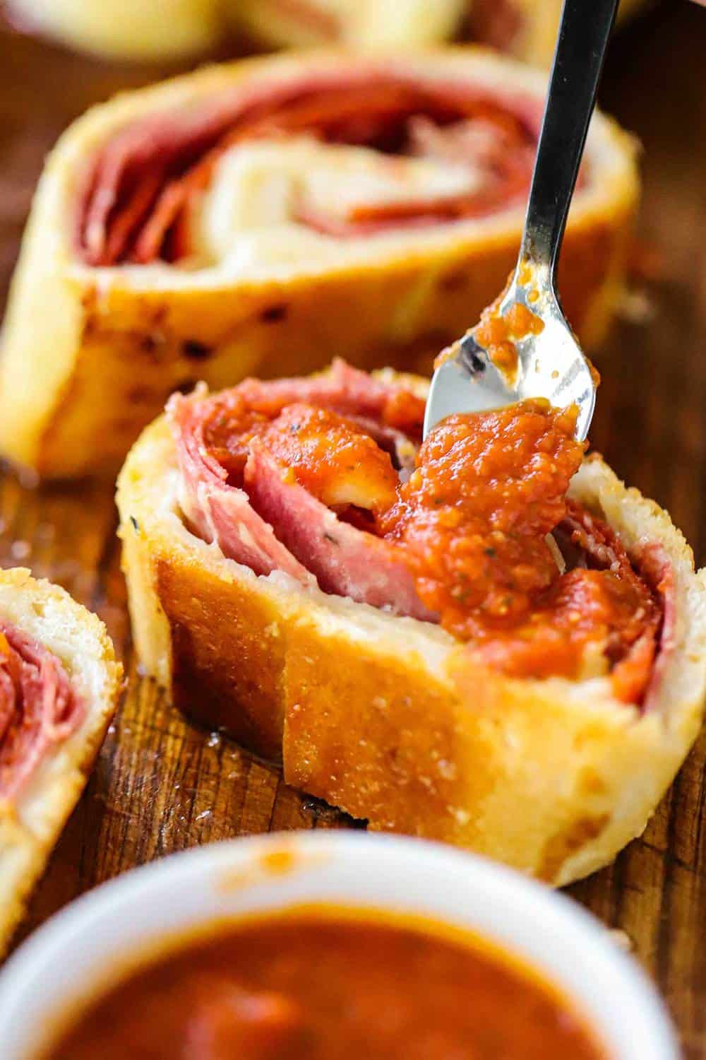 A small spoon being used to place marinara sauce on a slice of stromboli