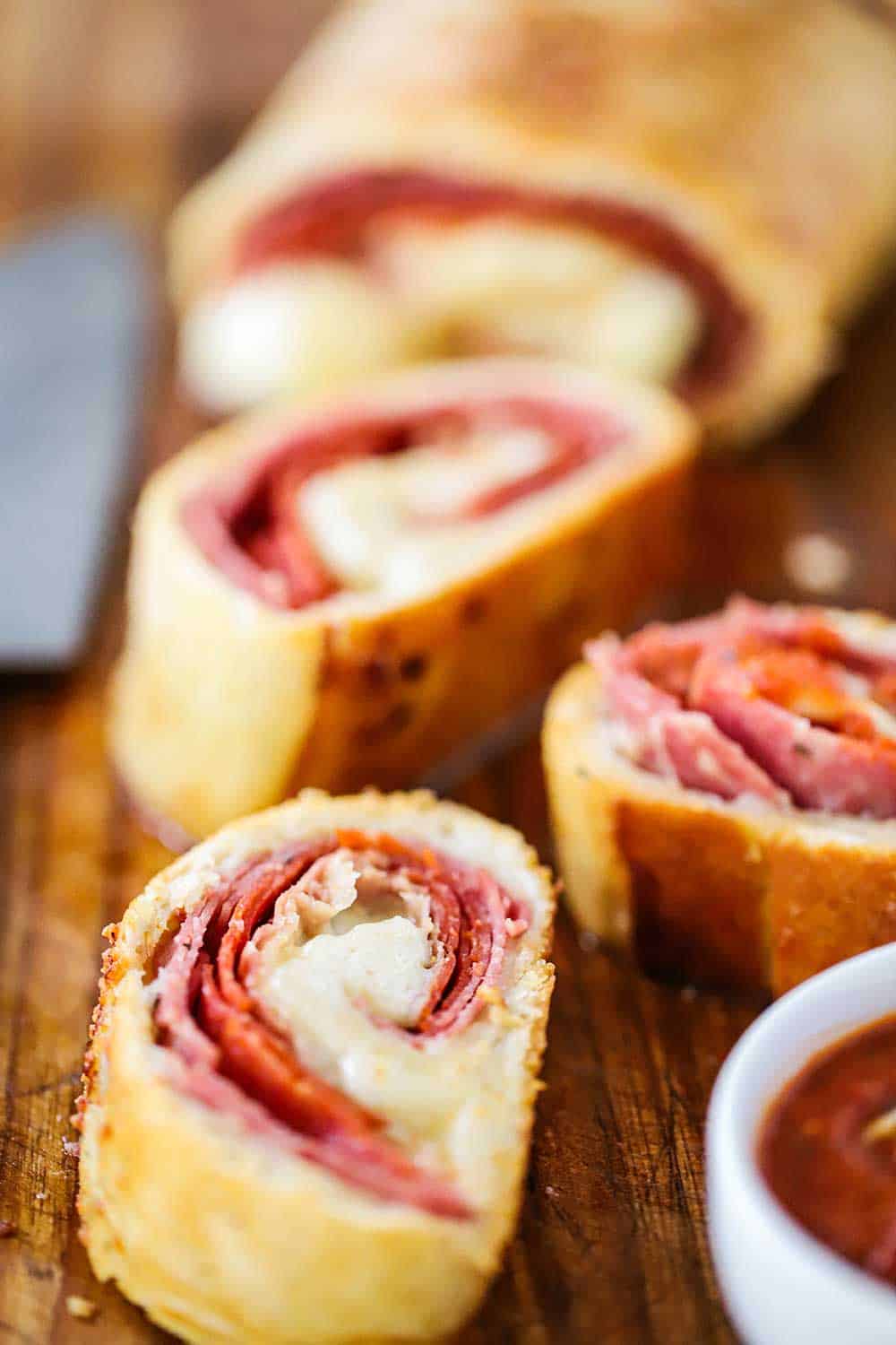 Several slices of homemade stromboli on a cutting board next to a chef's knife.