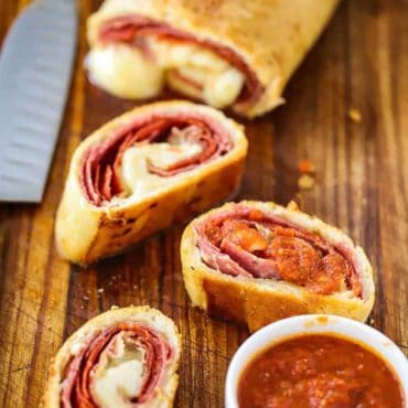 A stromboli sitting on a cutting board next to a knife with several slices of the stromboli in the foreground.