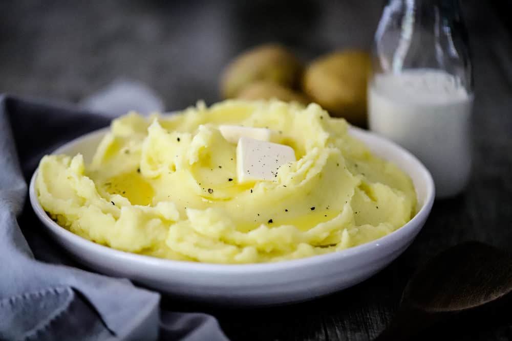 A bowl of mashed potatoes with melted butter on top and a bottle of cream nearby. 