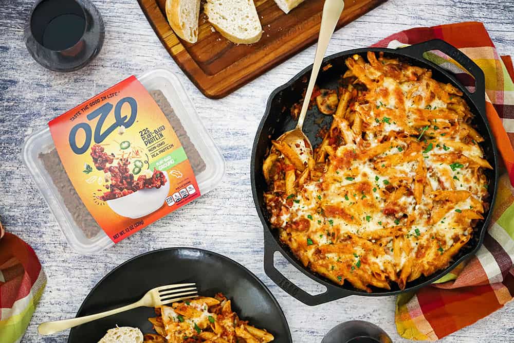 A cast-iron skillet filled with vegetarian pasta bake next to a package of OZO ground protein. 