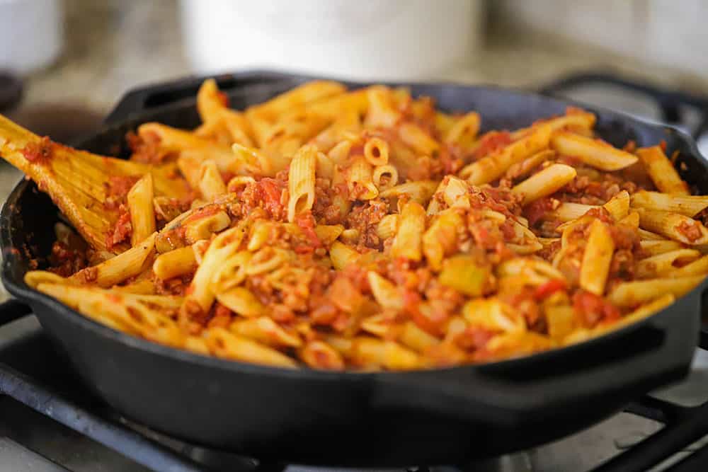 A cast-iron skillet filled with pasta in a vegetable sauce. 