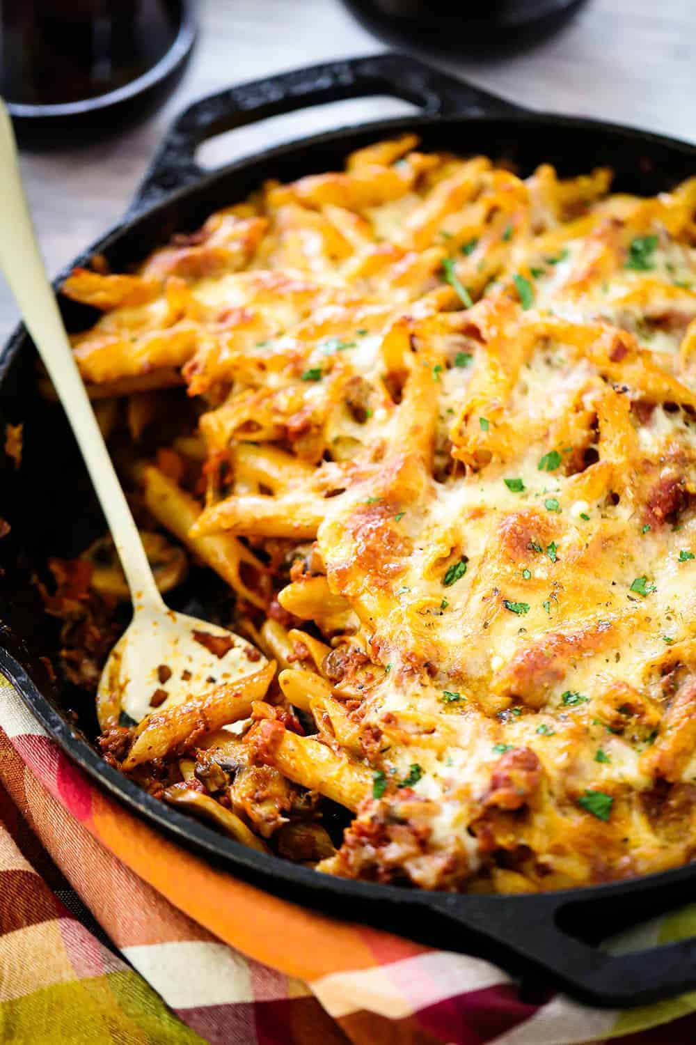 A large cast-iron skillet filled with vegetarian pasta bake with a spoon in it. 