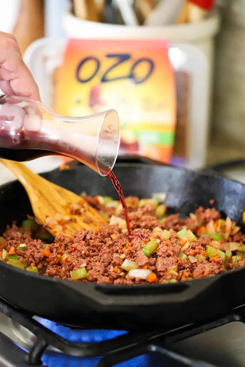 Red wine pouring from a small carafe into a skillet of ground plant-based protein and sautéed vegetables. 