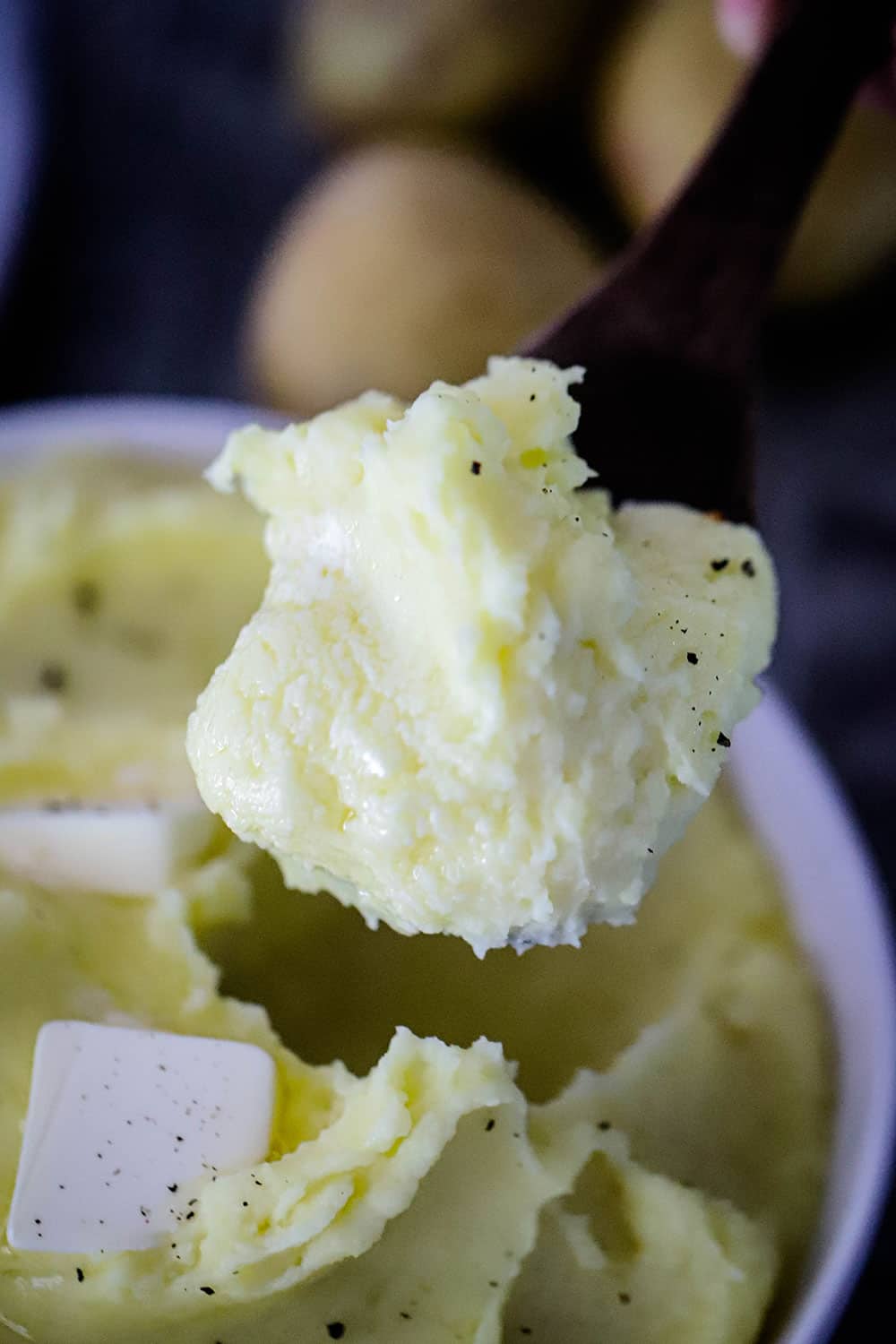 A large wooden spoon holding up a big helping of creamy mashed potatoes. 