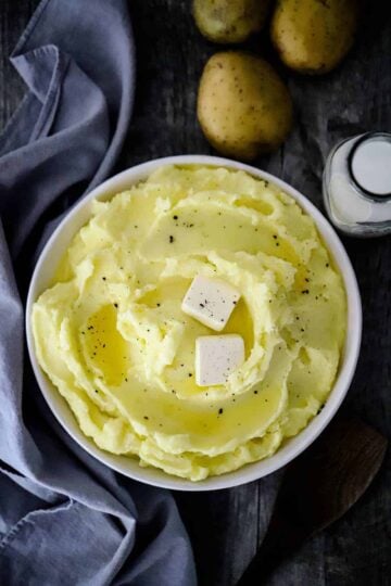 A large circular bowl filled with mashed potatoes with melted butter on top.