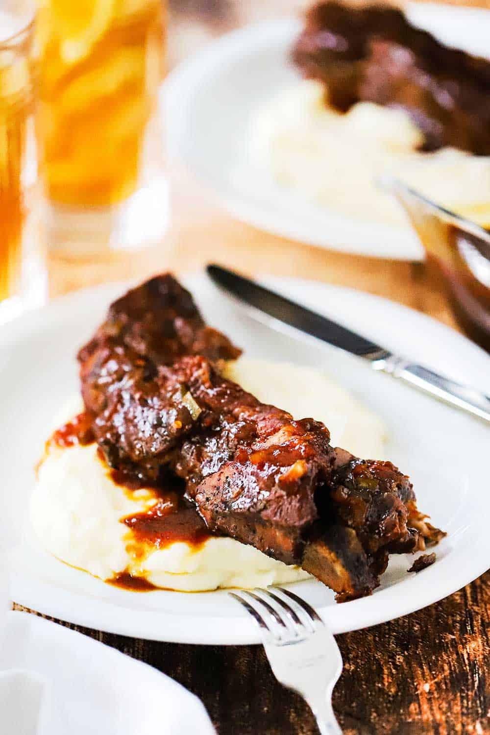 A white plate filled with a serving of mashed potatoes with a country-style ribs and sauce on top of it. 