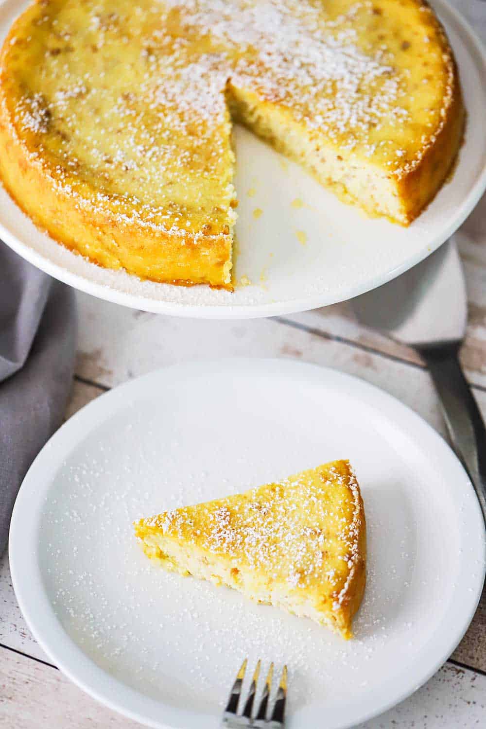 An Italian ricotta cheesecake on a cake stand with a slice of the cake on a plate next to it. 