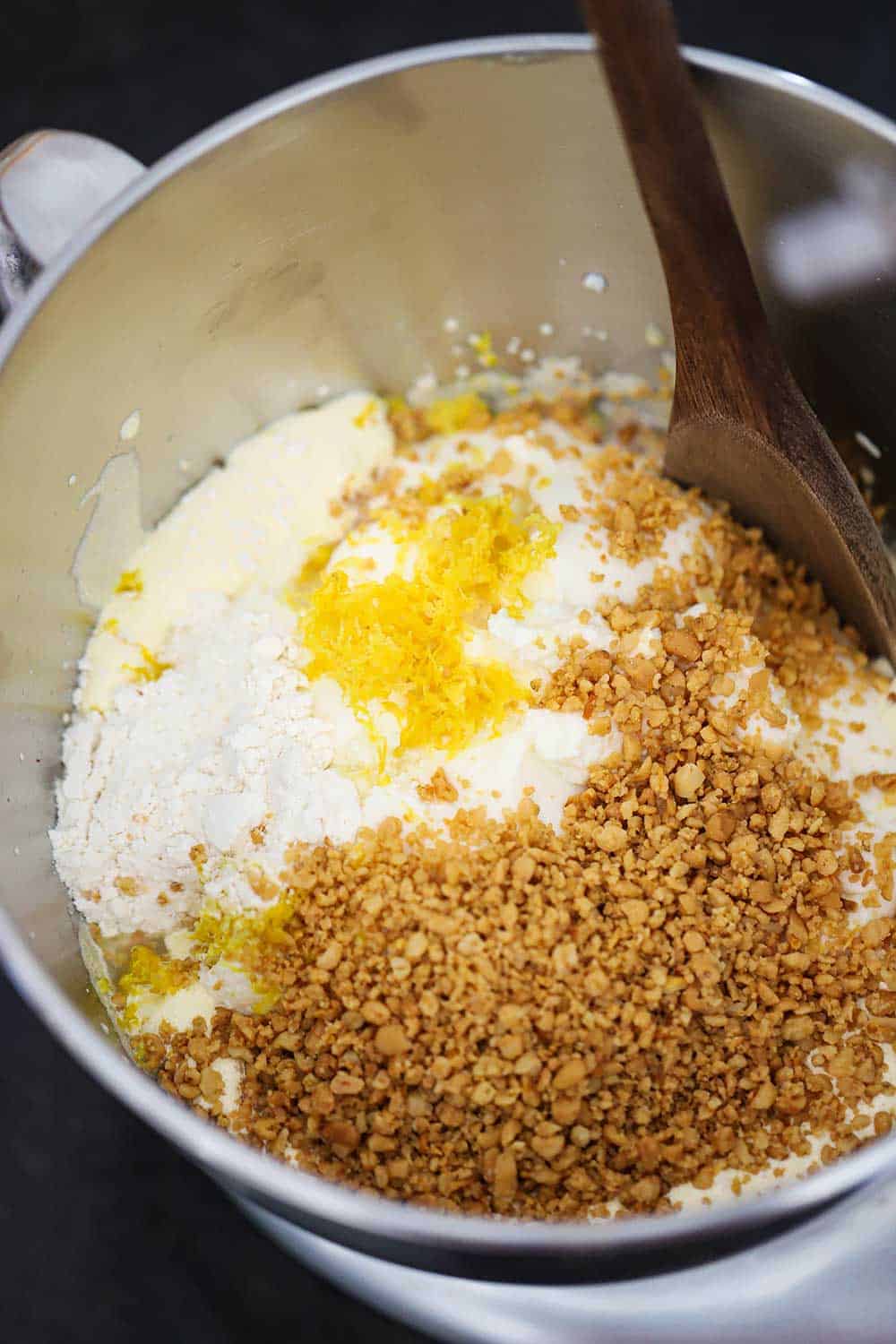 A mixer bowl filled with crushed pine nuts, lemon zest, and ricotta cheese. 