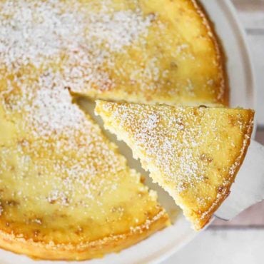 A slice of Italian ricotta cheesecake being lifted out of the cake on a cake stand.