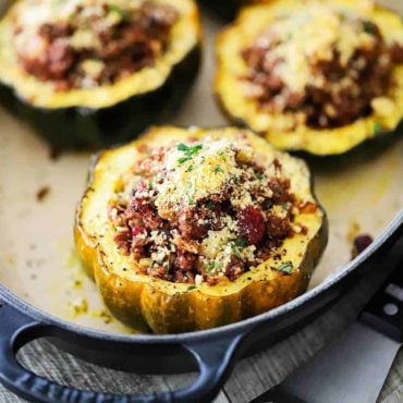 4 stuffed acorn squash filled with a vegetarian stuffing all in a oval baking dish.