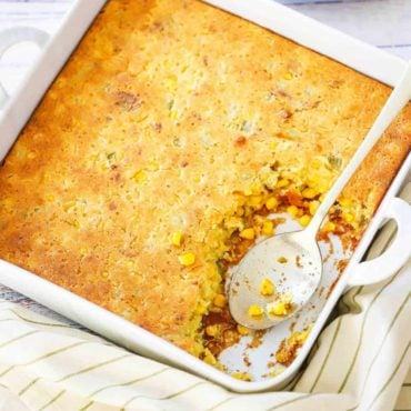 A square white baking dish filled with corn casserole next to a plate filled with the same.