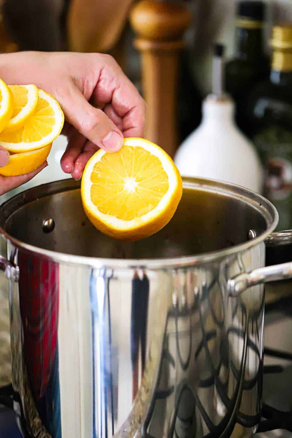 A hand dropping an orange slice into a large silver pot on the stove.