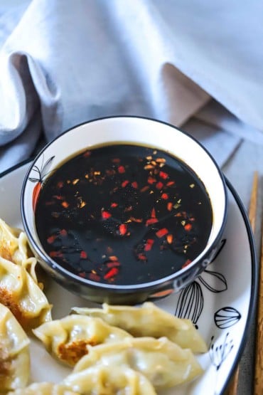 A bowl filled with ginger-soy dipping sauce on a platter of potstickers.