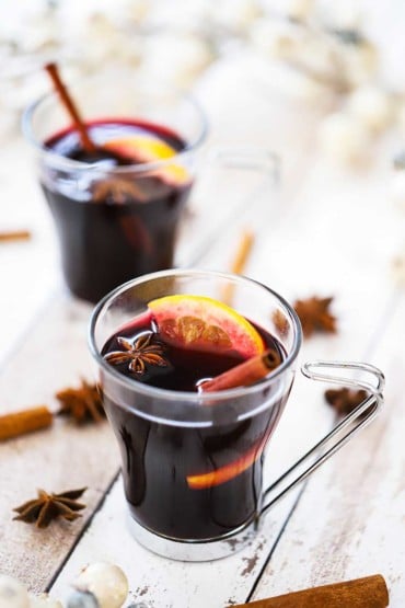Two clear glasses filled with mulled wine and garnished with a cinnamon stick, star anise, and an orange slice.