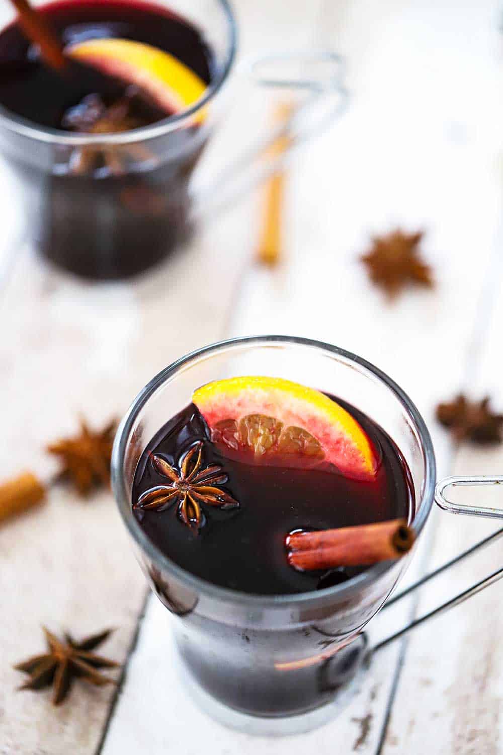 A clear glass filled with mulled wine garnished with star anise, a cinnamon stick, and an orange slice.