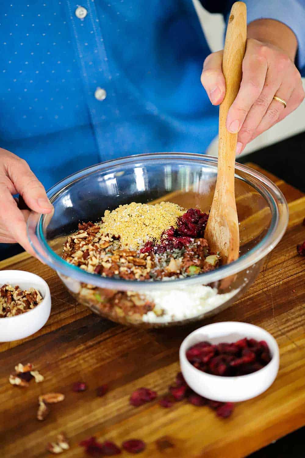 A person mixing together with a wooden spoon in a glass bowl all the ingredients for filling roasted acorn squash. 