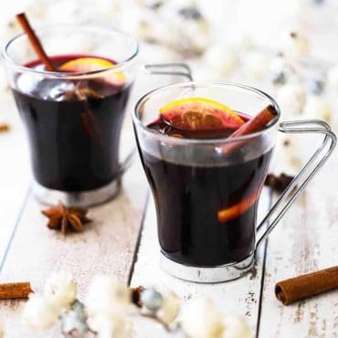 Two clear glasses filled with mulled wine and garnished with a cinnamon stick, star anise, and an orange slice.