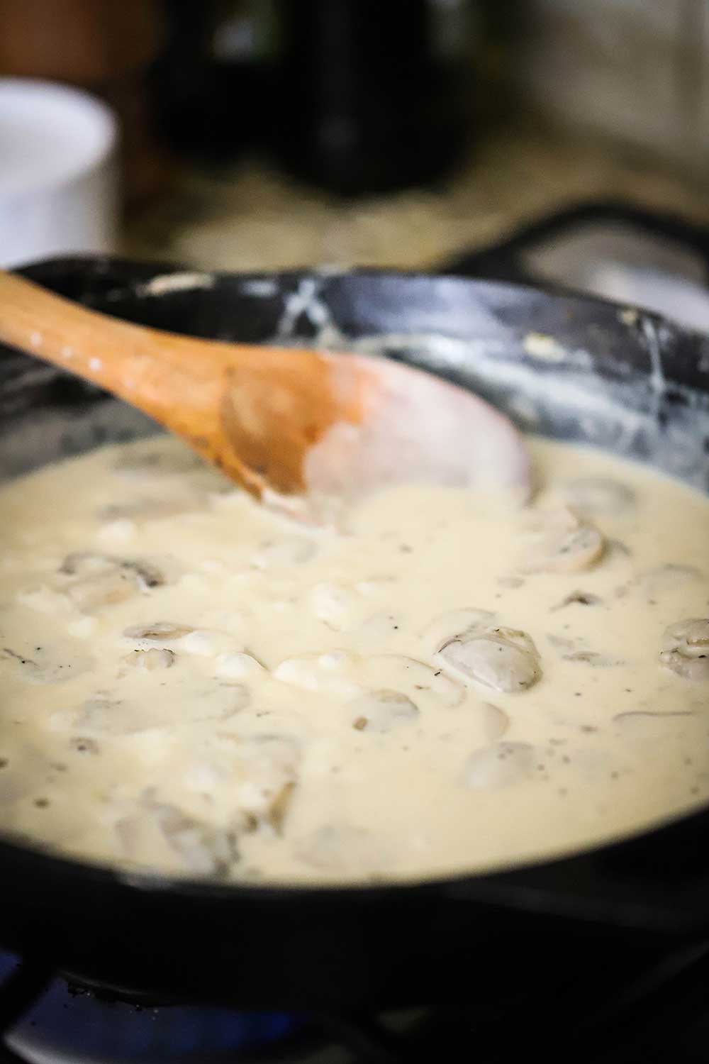 A cast-iron skillet filled with a cream sauce and sautéd sliced mushrooms.