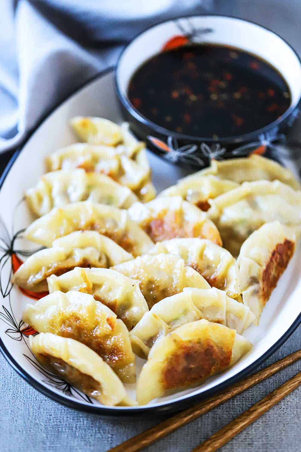 A platter of potstickers next to a bowl of dipping sauce.