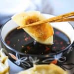 A potsticker being dunked into a bowl with chop sticks into a bowl of soy dipping sauce