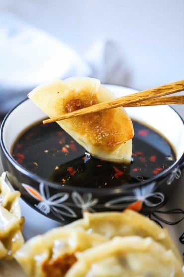 A potsticker being dunked into a bowl with chop sticks into a bowl of soy dipping sauce