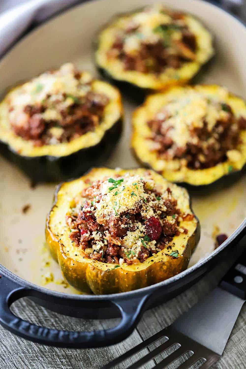 4 stuffed acorn squash filled with a vegetarian stuffing all in a oval baking dish. 