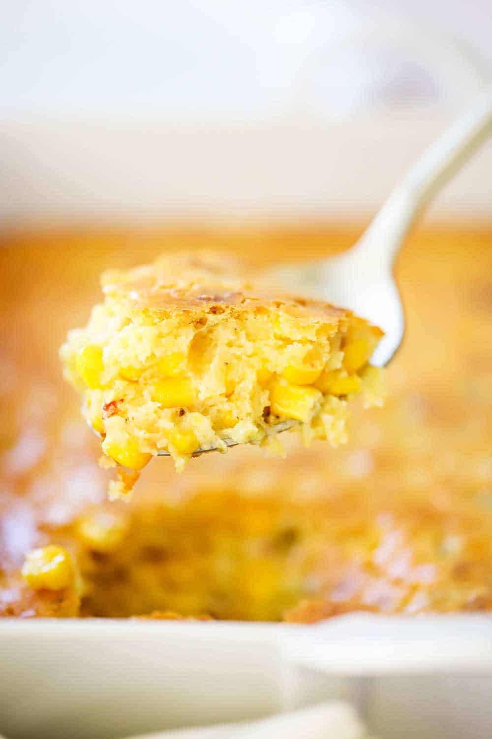 A gold serving spoon holding up a large scoop of corn casserole. 