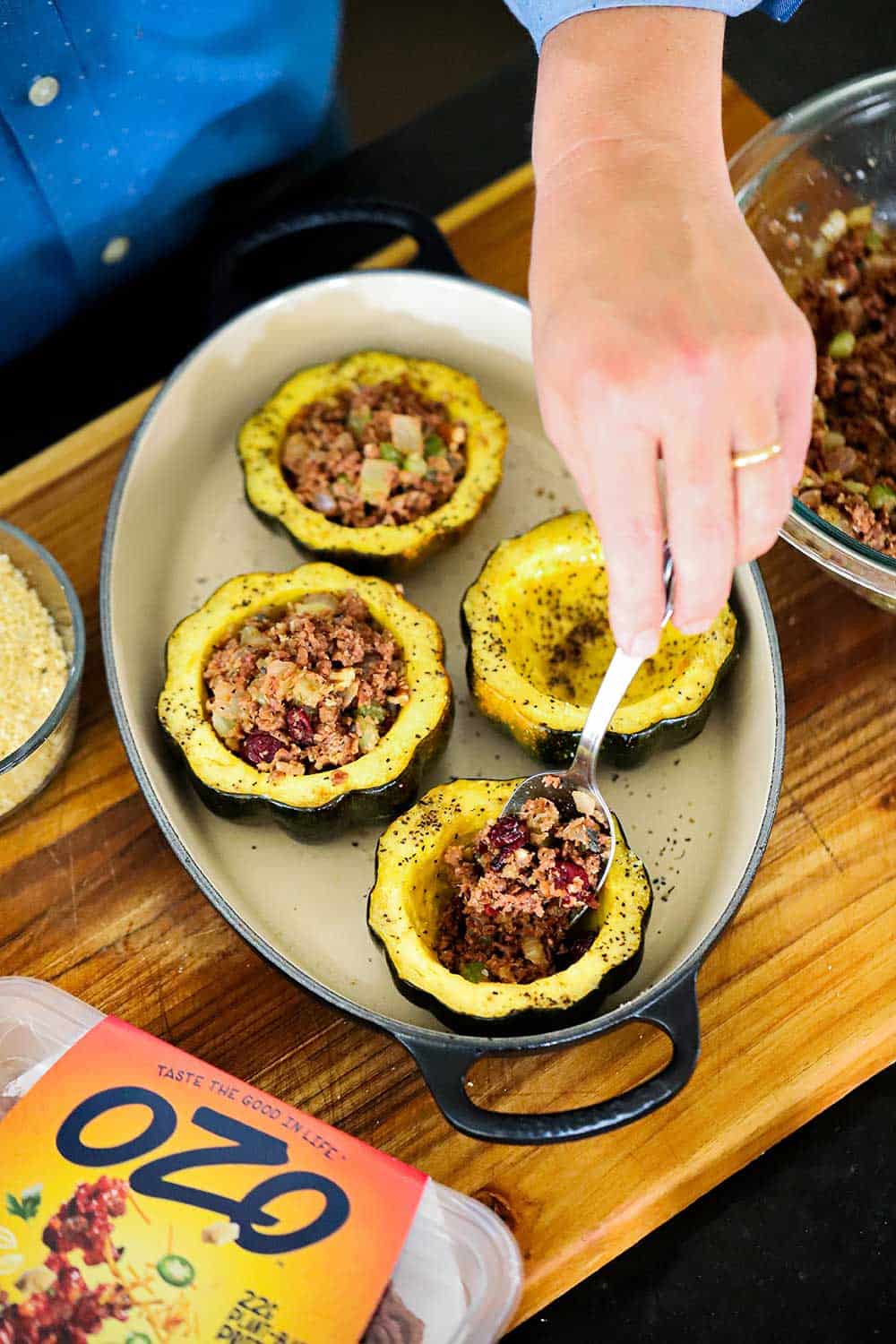 A person using a spoon to stuff roasted acorn squash in a baking dish. 