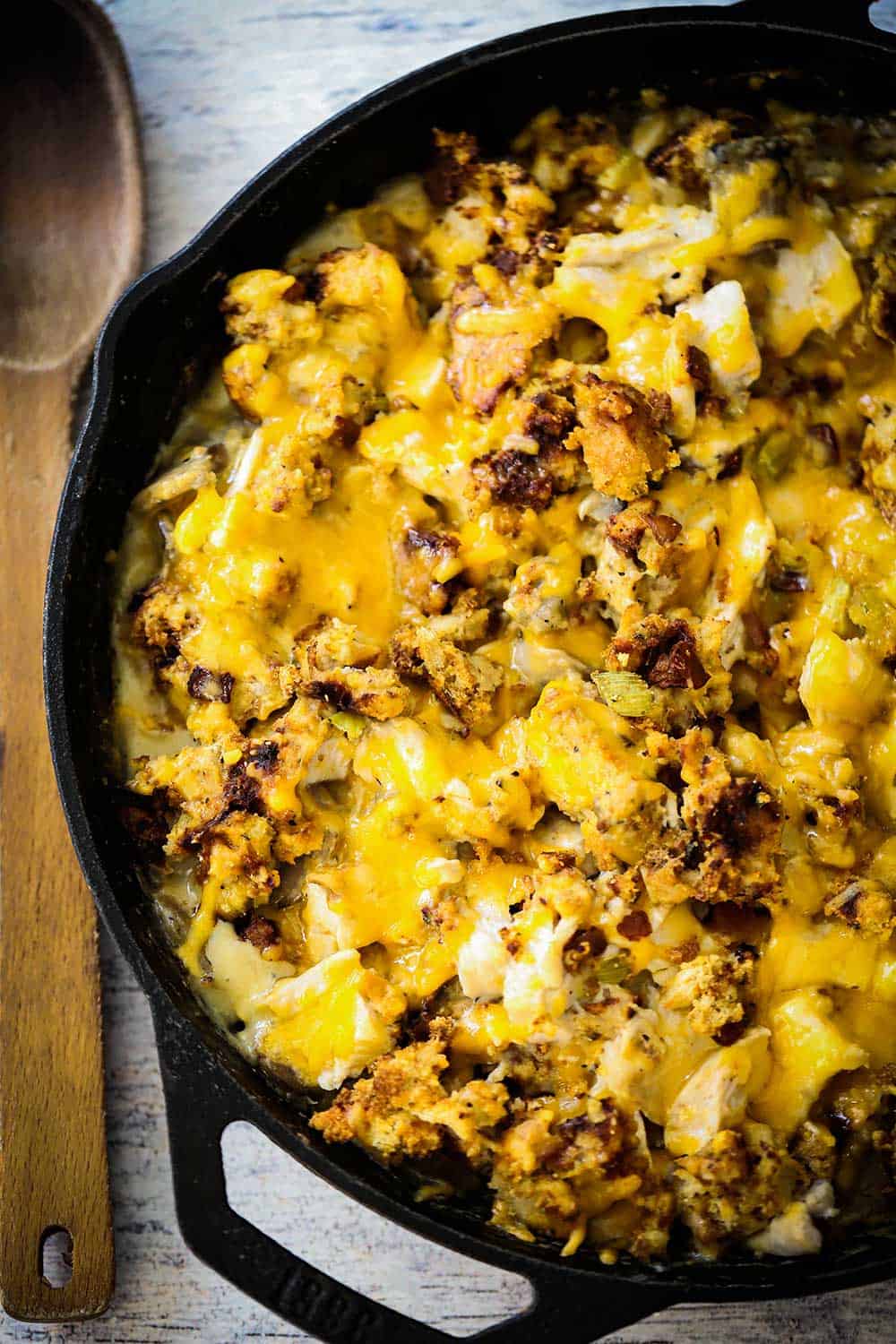 A large black cast-iron skillet filled with a cheesy turkey and stuffing dressing all sitting next to a large wooden spoon.