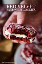 A hand holding a red velvet sandwich cookie with a bite take out of it.