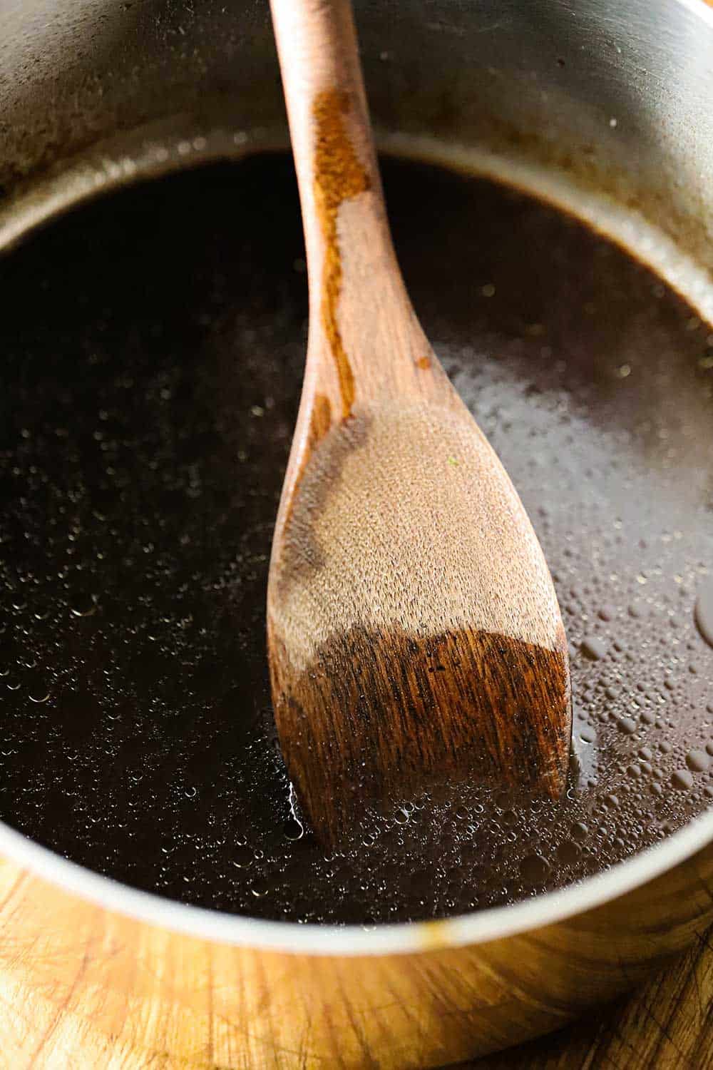 A saucepan filled with homemade au jus sauce with a wooden spoon in it. 