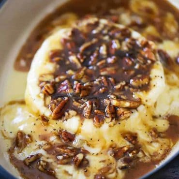 A wheel of baked brie in a baking dish smothered in pecan praline sauce.