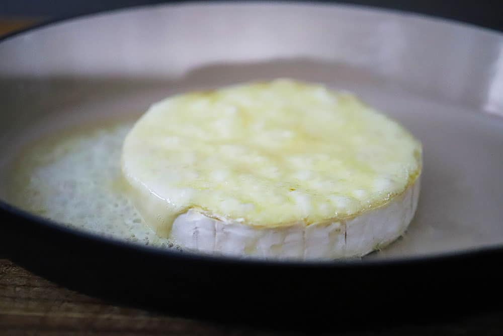 A wheel of brie that has been baked in a baking dish and is bubbling on the surface. 