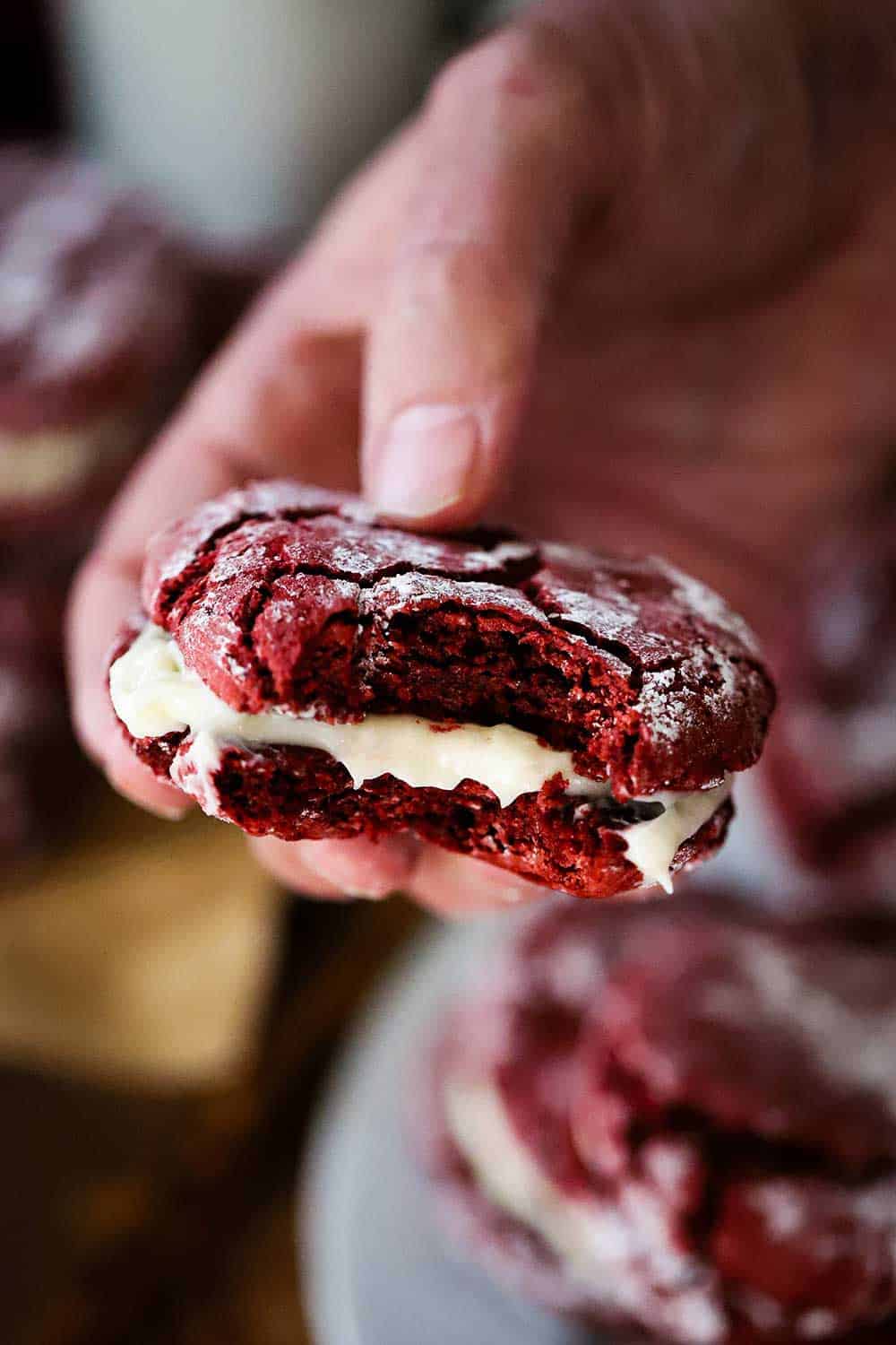 A hand holding a red velvet sandwich cookie with a bite take out of it. 