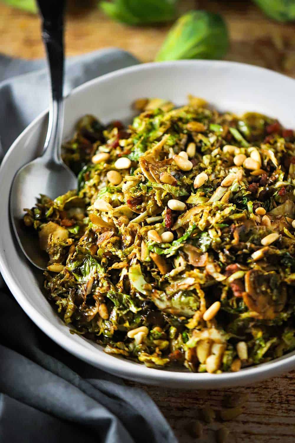 A large circular white serving dish filled with shaved Brussels sprouts with pancetta and balsamic. 