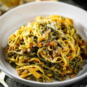 A white individual serving bowl filled with fettuccine with creamy sausage sauce.