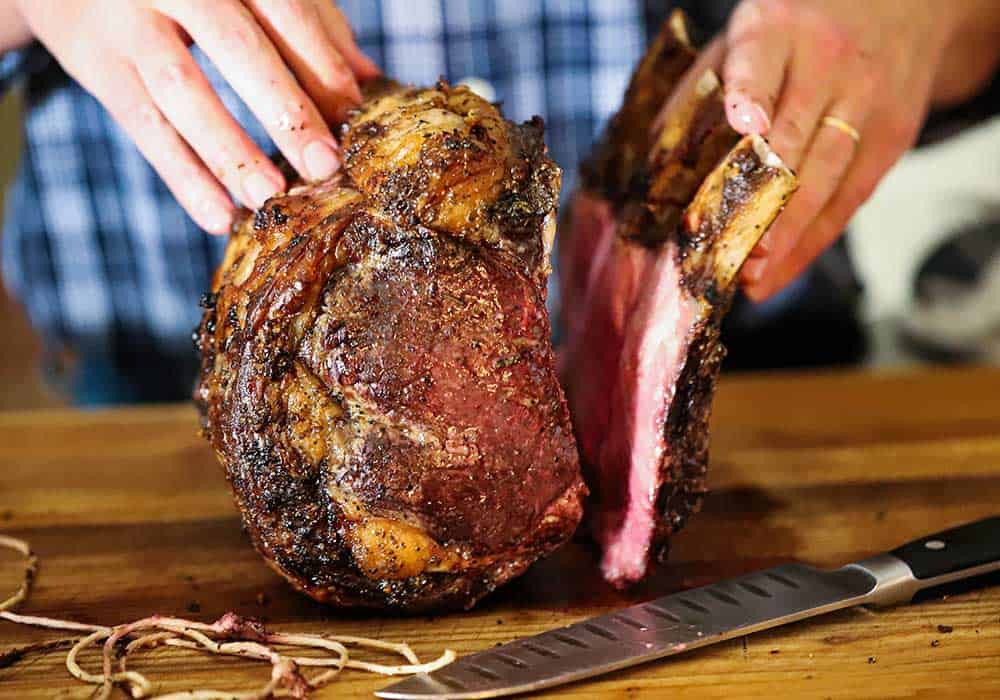 A person pulling the bones away from a prime rib roast that have been held in place by kitchen twine. 