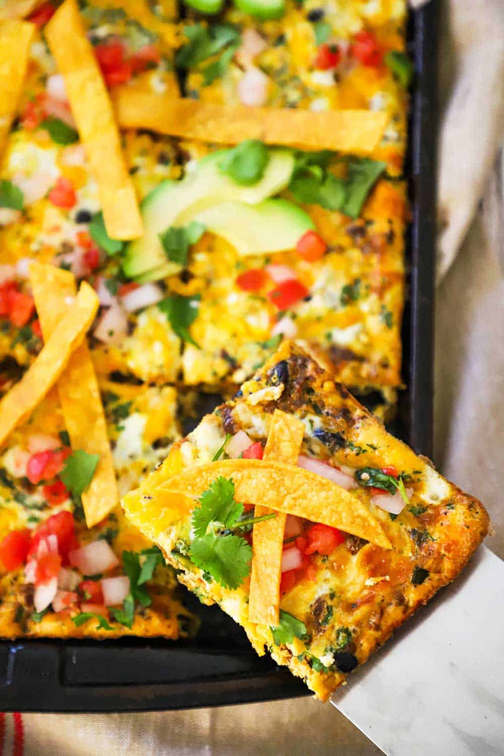 A slice of a Mexican frittata being lifted out of a sheet pan of the dish. 