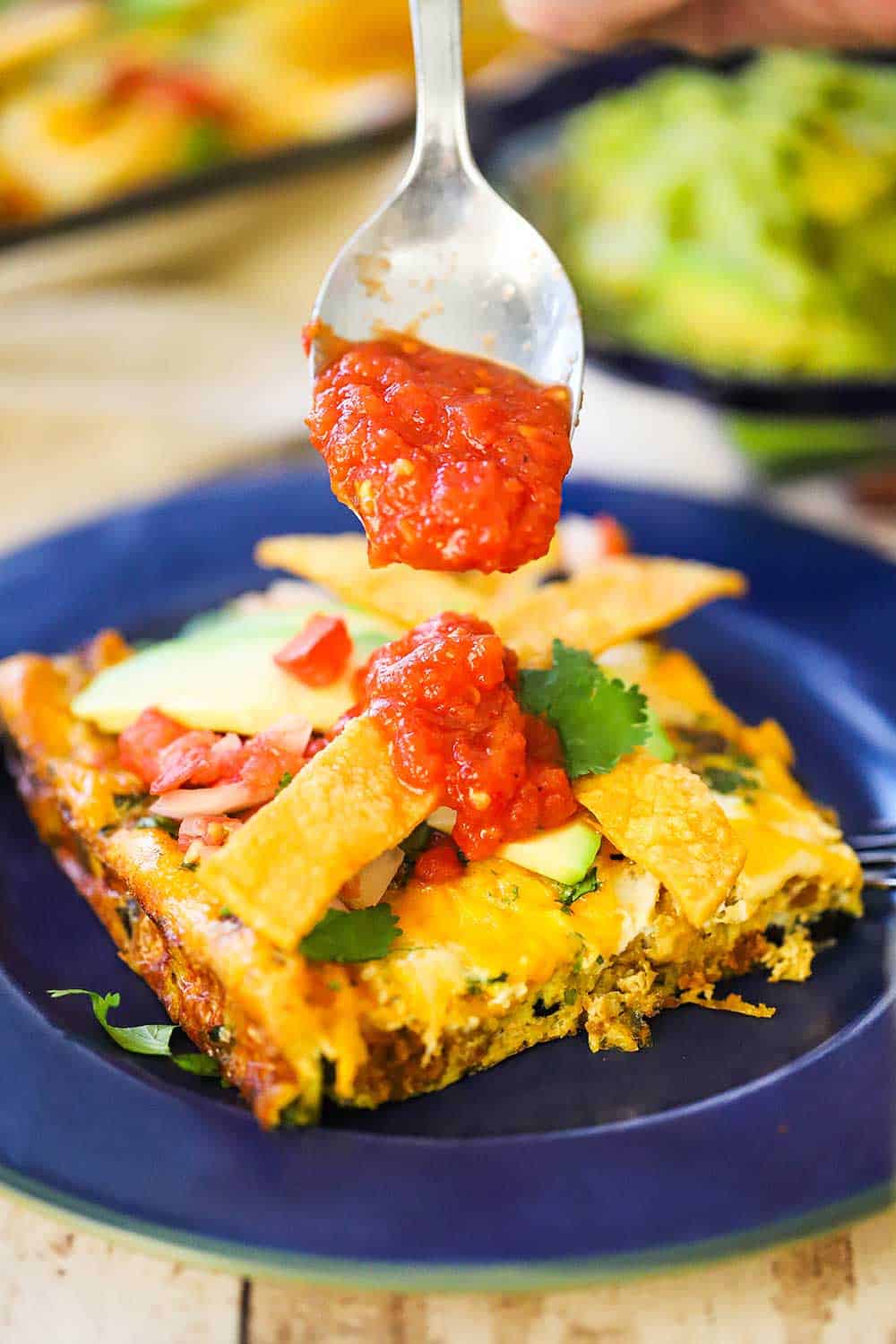 Fresh salsa being drizzled over a slice of Mexican frittata that is sitting on a blue plate. 