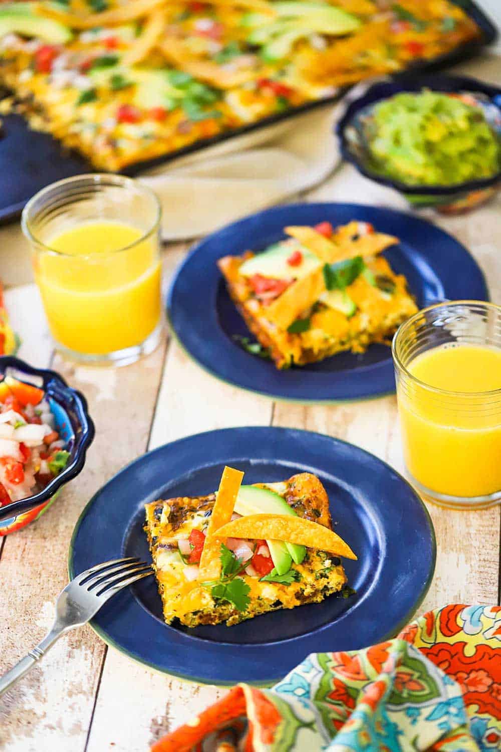 Mexican frittata squares on a couple of blue plates next to glasses of orange juice. 