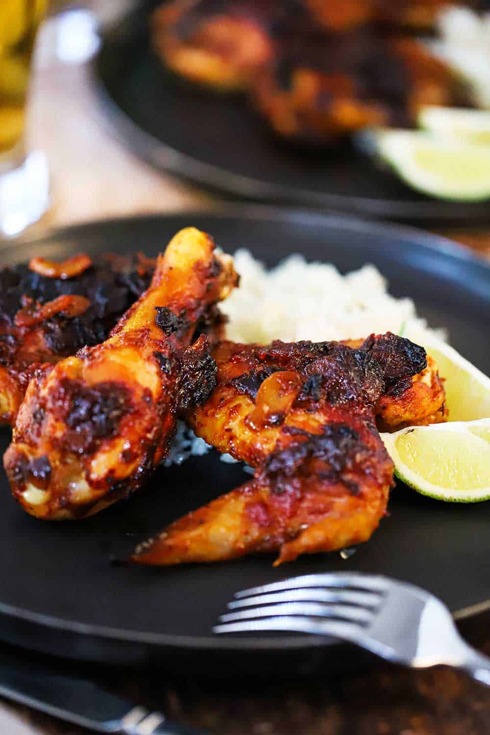 A black dinner plate filled with two pieces of roasted chipotle chicken, cilantro-lime rice, and 2 lime wedges, all sitting next to a glass of Mexican beer.