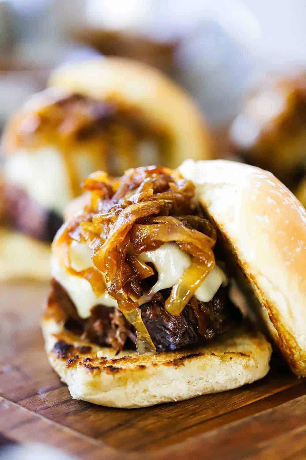 A leftover pot roast slider sitting on a cutting board that is topped with a mound of caramelized onions and melted Swiss cheese. 